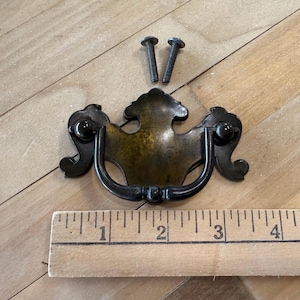 May include: An antique brass drawer pull with a decorative design, featuring a curved handle and two screws. The pull is approximately 4 inches wide, with a vintage aesthetic, suitable for furniture restoration projects.