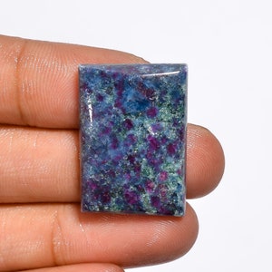May include: A rectangular gemstone with a polished surface. The stone features a mix of colors, including deep blue, green, and vibrant red. The red appears in small, irregular clusters throughout the stone. The overall effect is a textured, colorful appearance.