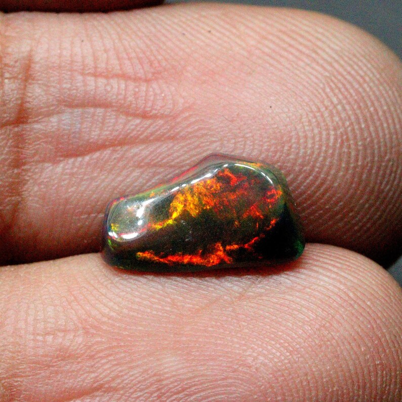 May include: A dark, iridescent black opal gemstone with flashes of red, orange, and green.