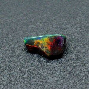 May include: A dark, iridescent black opal gemstone with flashes of green, yellow, and red.