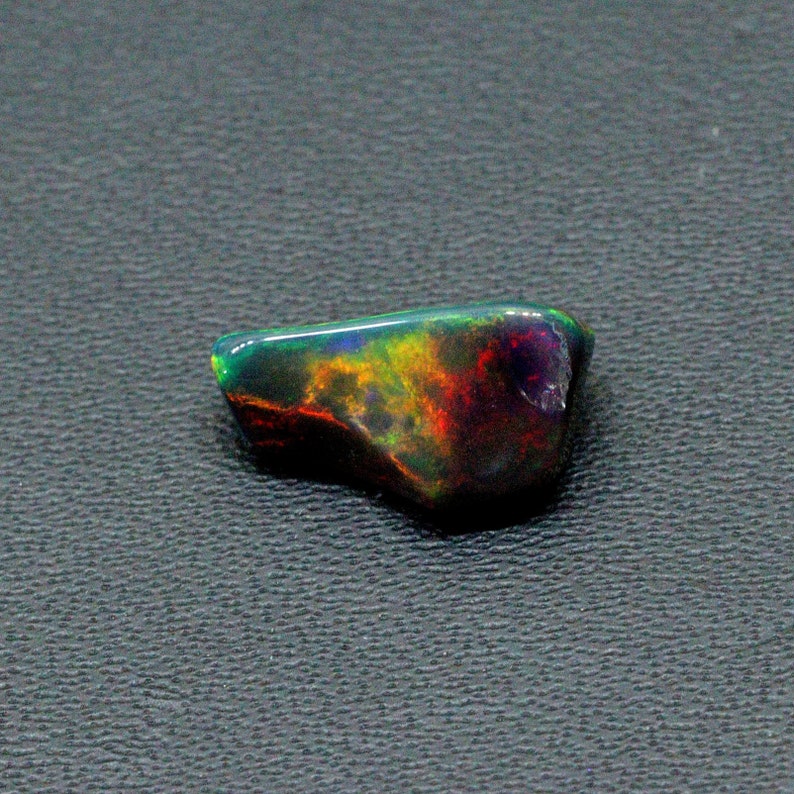 May include: A dark, iridescent black opal gemstone with flashes of green, yellow, and red.