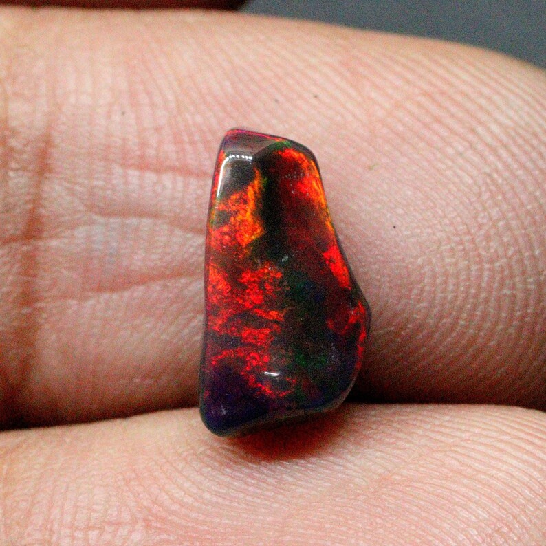 May include: A dark red, green, and black opal gemstone with a rough, irregular shape.