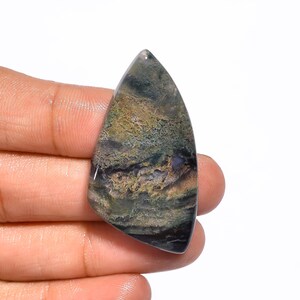 Peut inclure: Un cabochon d'agate vert, brun et gris de forme pointue. La pierre présente un motif tourbillonnant et est translucide.