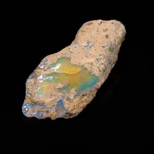 Puede incluir: Una roca áspera, marrón y gris con un parche de ópalo iridiscente que muestra colores verde, azul y amarillo.