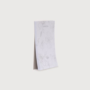 以下が含まれることがあります： 花柄のデザインが施された白いメモ帳で、前面に「NOTES」と印刷されています。