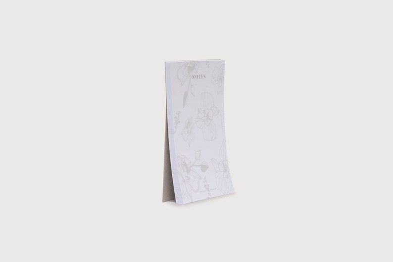 以下が含まれることがあります： 花柄のデザインが施された白いメモ帳で、前面に「NOTES」と印刷されています。