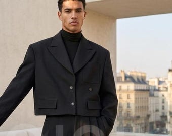 May include: A black cropped blazer with two buttons, paired with wide-leg trousers. The outfit includes a black turtleneck. The model is standing outdoors with a city backdrop.