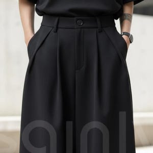 May include: Black wide-leg pants with a high waist and pleats. The pants have side pockets and a button closure. The fabric appears to be a smooth, solid color. The pants are part of a clothing collection.