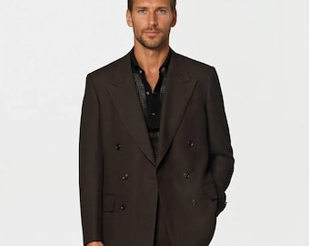 May include: A dark brown double-breasted suit with a black shirt. The suit has a classic design with a notched lapel and multiple buttons. The pants are straight-legged. The man is standing in front of a white background.