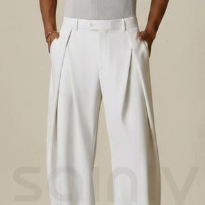 Puede incluir: Pantalones blancos plisados con pernera ancha. Los pantalones de cintura alta tienen bolsillos y se llevan con zapatos marrones. La tela parece lisa. El estilo es clásico y elegante. Los pantalones miden unos 100 cm de largo.