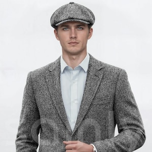 Può includere: Un blazer grigio a spina di pesce e un berretto abbinato. La giacca ha una classica chiusura a due bottoni e revers a lancia. L'outfit è completato da una camicia azzurra e un orologio d'argento.