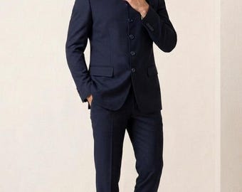 Puede incluir: Un traje azul marino oscuro que consta de una chaqueta con cuello mao, cinco botones frontales y dos bolsillos con solapa, combinado con pantalones a juego y zapatos de vestir de cuero marrón oscuro. El conjunto es liso y estructurado.