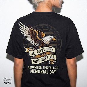 May include: Black t-shirt with a detailed eagle graphic, banner text reading "ALL GAVE SOME, SOME GAVE ALL," and the words "REMEMBER THE FALLEN MEMORIAL DAY." The design incorporates elements of the American flag.