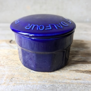 May include: A small, round, blue ceramic container with a lid. The lid has the words "DALFOUR" embossed on it.