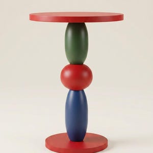 Può includere: Un tavolino con piano e base circolari rossi, collegati da una colonna centrale composta da tre forme arrotondate impilate in verde, rosso e blu. La struttura è liscia e simmetrica, con una finitura opaca uniforme su tutto il pezzo.