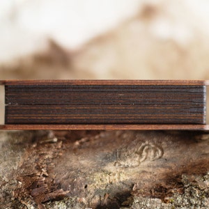 Op de afbeelding: Een kleine, rechthoekige houten doos met een donkerbruin interieur en een lichtere bruine lijst. De doos rust op een getextureerd, natuurlijk houten oppervlak, met een vage achtergrond.