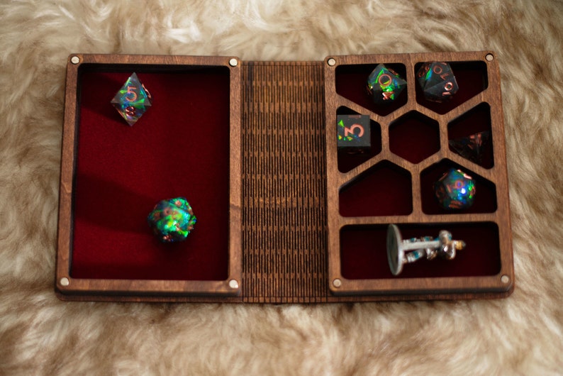 Op de afbeelding: Een houten dobbeldoos met een rode fluwelen binnenkant, met verschillende iriserende dobbelstenen en een miniatuurbeeldje. De doos is open, met compartimenten voor de dobbelstenen en een decoratief ontwerp op het deksel.