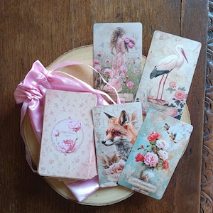 Peut inclure: Un jeu de cartes oracle avec des illustrations de style vintage représentant une femme, une cigogne, un renard et un vase floral, accompagné d'une pochette en satin rose. Les cartes portent les inscriptions 29 Femme, 17 Cigogne, 14 et 12 Oiseaux.