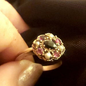 May include: A gold ring featuring a black gemstone surrounded by pink and white gemstones.