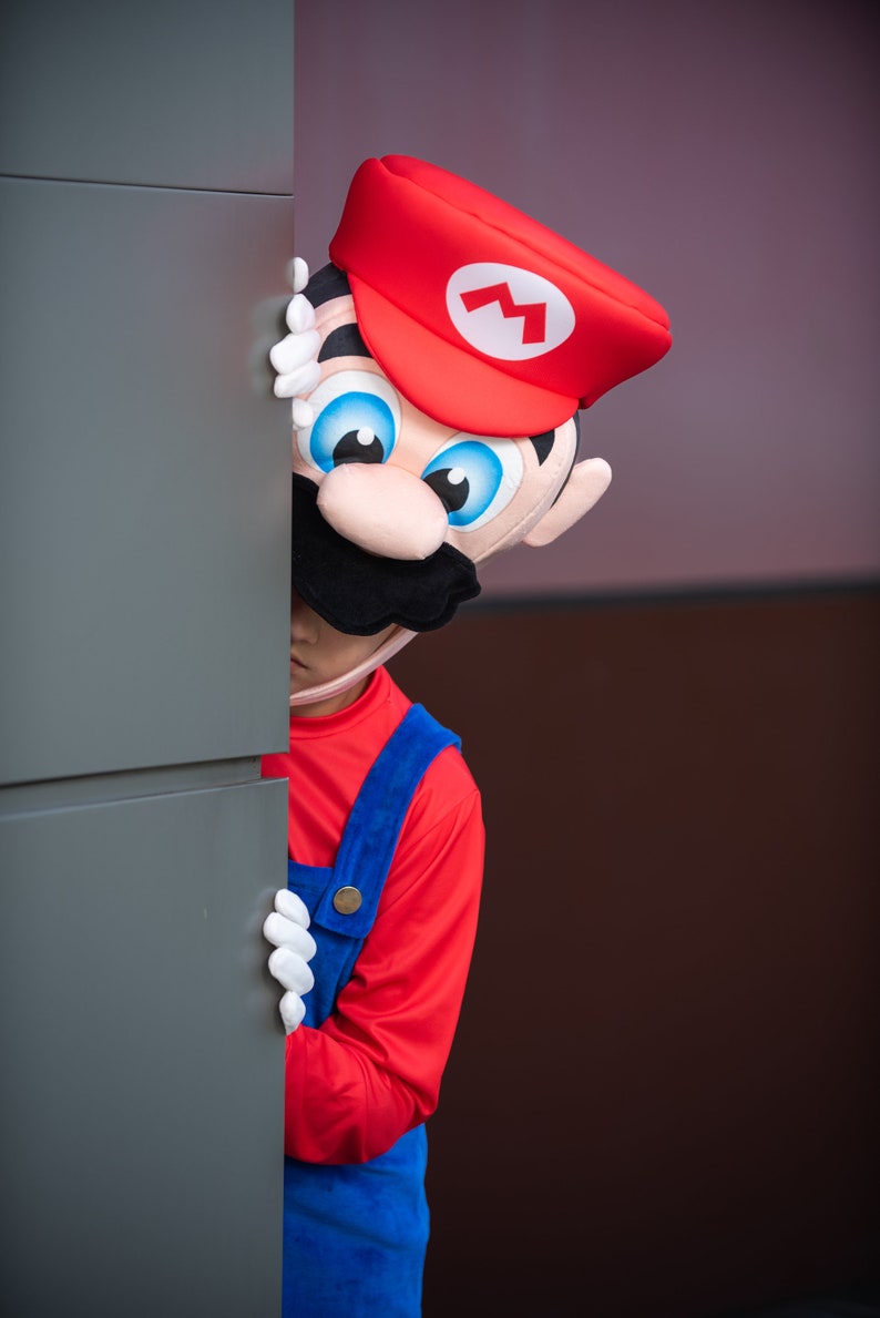 Op de afbeelding: Een persoon verkleed als Mario uit de Super Mario-videogameserie kijkt om een hoek. Het kostuum is rood en blauw met een witte bliksem op de hoed.