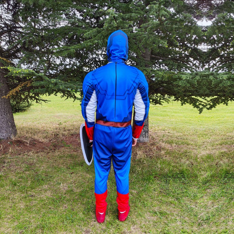 May include: A blue Captain America costume with a hood, white and red accents, and a brown belt. The costume includes matching blue trousers and red boots. A shield is held on the left side.