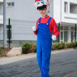 Op de afbeelding: Een kind verkleed als Super Mario, met een rood-witte hoed met snor en een blauwe overall. Het kind loopt op een stoep.