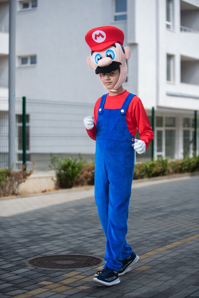 Op de afbeelding: Een kind verkleed als Super Mario, met een rood-witte hoed met snor en een blauwe overall. Het kind loopt op een stoep.