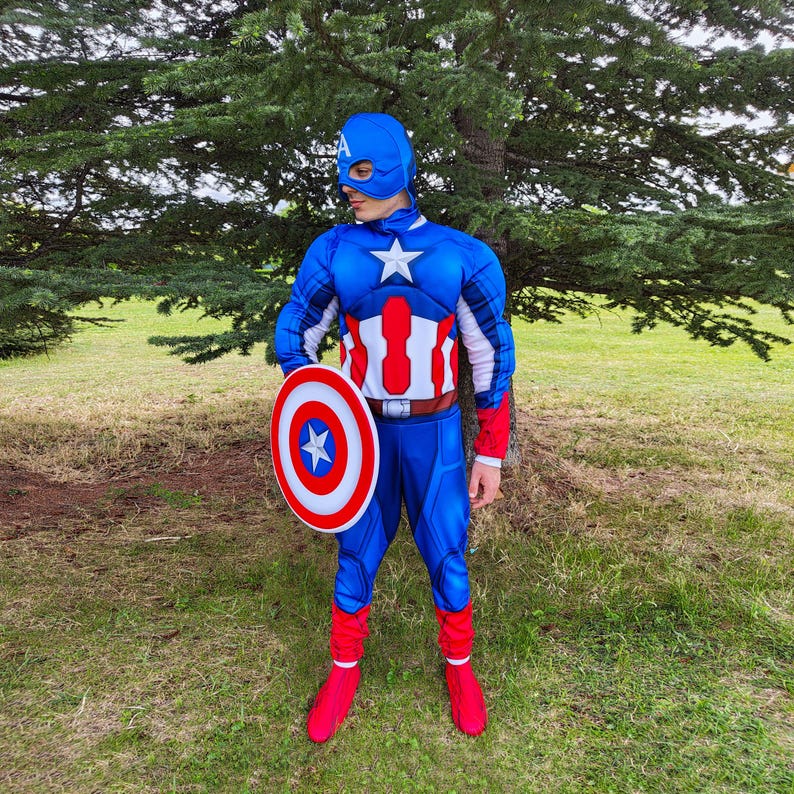 May include: A blue Captain America costume with a white star on the chest and a matching shield. The costume includes a blue mask, gloves, and boots. The shield is red, white, and blue with a star in the centre.