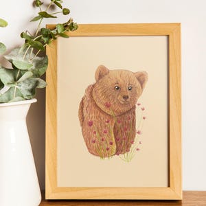 Peut inclure: Illustration encadrée d'un ours brun entouré de fleurs roses et d'herbe verte. L'œuvre est dans un cadre en bois clair. Le fond est beige clair. Idéal pour une chambre d'enfant.