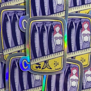 Peut inclure: Plusieurs autocollants holographiques représentant une boîte de sardines. Les autocollants montrent des sardines à l'huile d'olive, avec une illustration de sirène. Le texte "SA" et "IN OLIVE OIL" est visible.