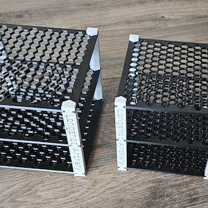 Puede incluir: Dos estantes de metal negro con un patrón de panal. Los estantes están hechos por "Lost in Architecture" y son de diferentes tamaños.