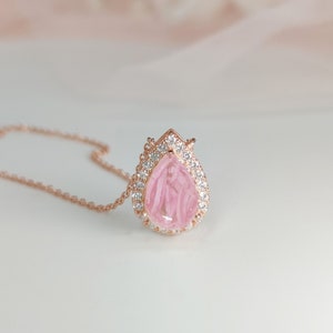 May include: A delicate rose gold necklace with a pear-shaped pink gemstone pendant surrounded by a halo of sparkling clear stones.