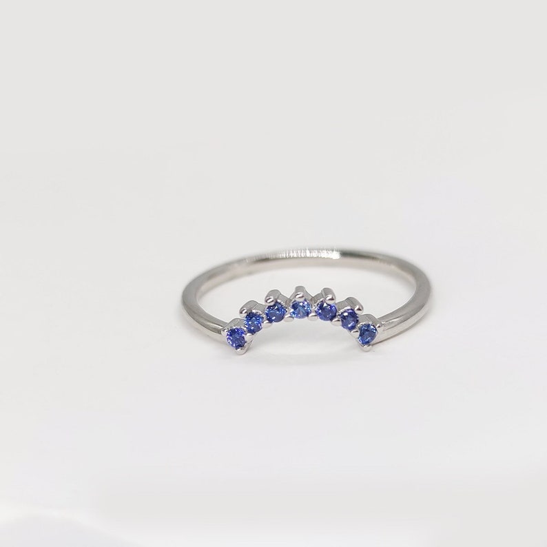 May include: A silver band ring with a row of small blue sapphires set in a curved arch shape.