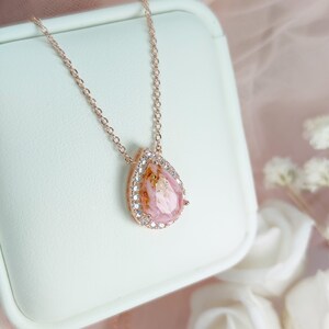 May include: A delicate rose gold necklace with a pear-shaped pink stone set in a clear crystal halo.