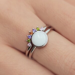 May include: A silver ring set with a white round stone and a rainbow of small colorful stones.