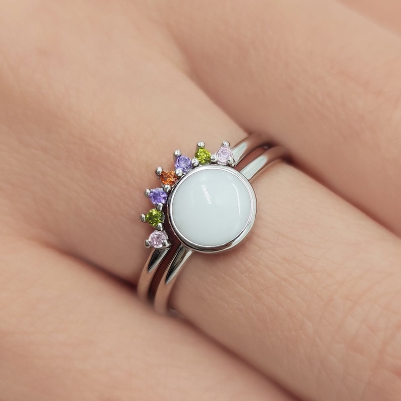 May include: A silver ring set with a white round stone and a rainbow of small colorful stones.