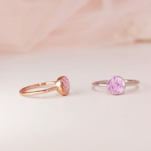 May include: Two delicate rings with pink floral resin inlays. The ring on the left is gold, and the ring on the right is silver.