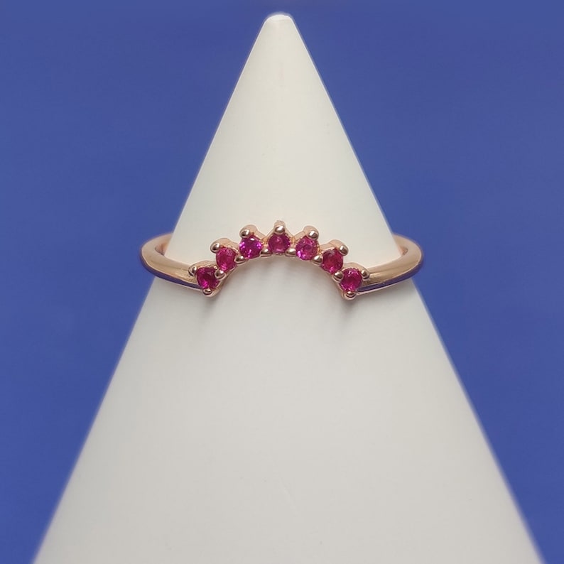 May include: A rose gold ring with a row of small pink gemstones set in a curved arch shape.