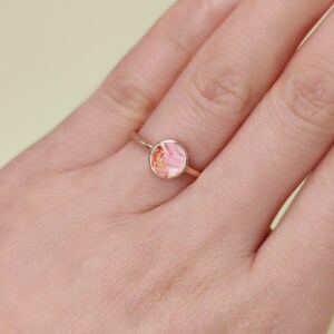 May include: A gold ring with a pink and orange marbled stone.