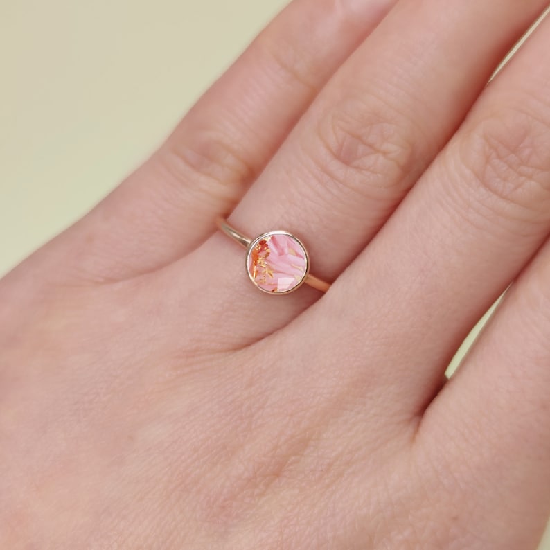 May include: A gold ring with a pink and orange marbled stone.
