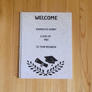May include: A spiral-bound notebook with a white cover featuring the word "WELCOME" in black. The cover also includes text that reads "RANDOLPH-HENRY CLASS OF 1987 35 YEAR REUNION" and a graduation-themed graphic.