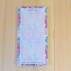 May include: A rectangular to-do list notepad featuring a floral border in shades of purple, pink, and teal. The center has a white area with the text TO DO LIST at the top, followed by lined checkboxes, and the text Believe...Celebrate...Reward...Set...Give.