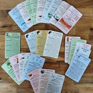 Peut inclure: Un ensemble de cartes colorées avec du texte et des illustrations, disposées sur une surface en bois. Les cartes présentent divers motifs, notamment des symboles, des diagrammes et du texte en français. Les cartes semblent liées à un thème spirituel ou de bien-être.