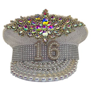 May include: White sequined hat with a large iridescent crystal embellishment on top and a pearl and rhinestone band with the number "16" in the centre.