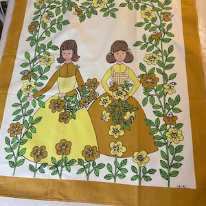Könnte beinhalten: Ein vintage Küchentuch mit einem gelben, grünen und weißen Blumendesign. Zwei Mädchen in gelben und braunen Kleidern halten Sträuße gelber Blumen. Der Text "ULLAS" ist in der rechten unteren Ecke gedruckt.
