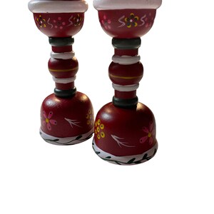 May include: A set of two red wooden candle holders with white and green painted details. The holders are decorated with pink and yellow flowers and have a traditional folk art style.