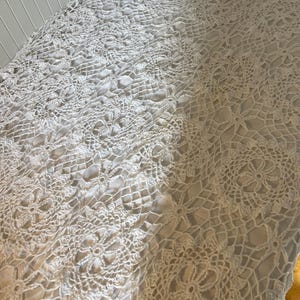 May include: White crocheted tablecloth with a delicate floral pattern. The tablecloth is made of a fine, lightweight yarn and has a soft, drapey texture.