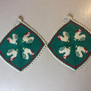 Puede incluir: Dos agarraderas de olla de crochet verde con pollos blancos y detalles rojos.