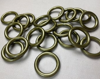 May include: A group of 18 gold-colored metal rings, likely curtain rings, are scattered on a white surface. The rings are all the same size and shape, and they are arranged in a random pattern.