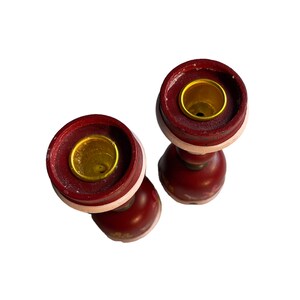 May include: Two red wooden candle holders with gold accents and floral designs. The candle holders are empty and ready to be used.